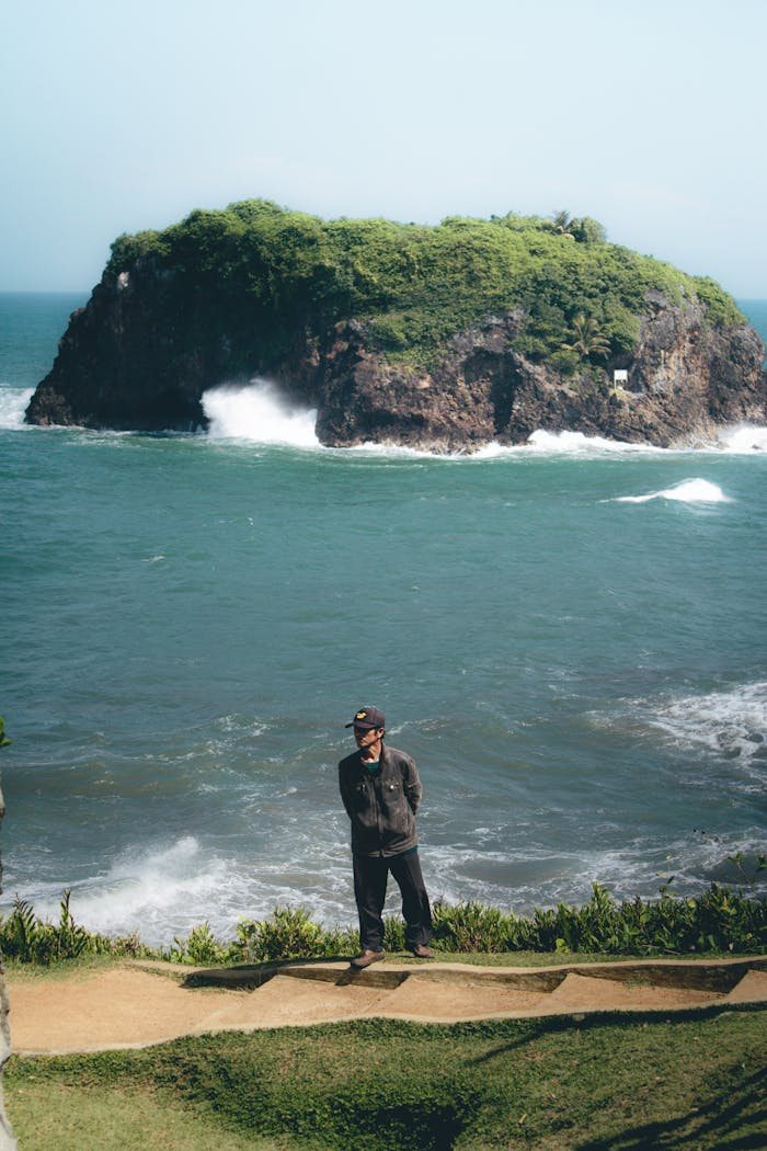 why-choose-us A man stands on a cliff overlooking the ocean with a lush island in the background, located in West Java, Indonesia.